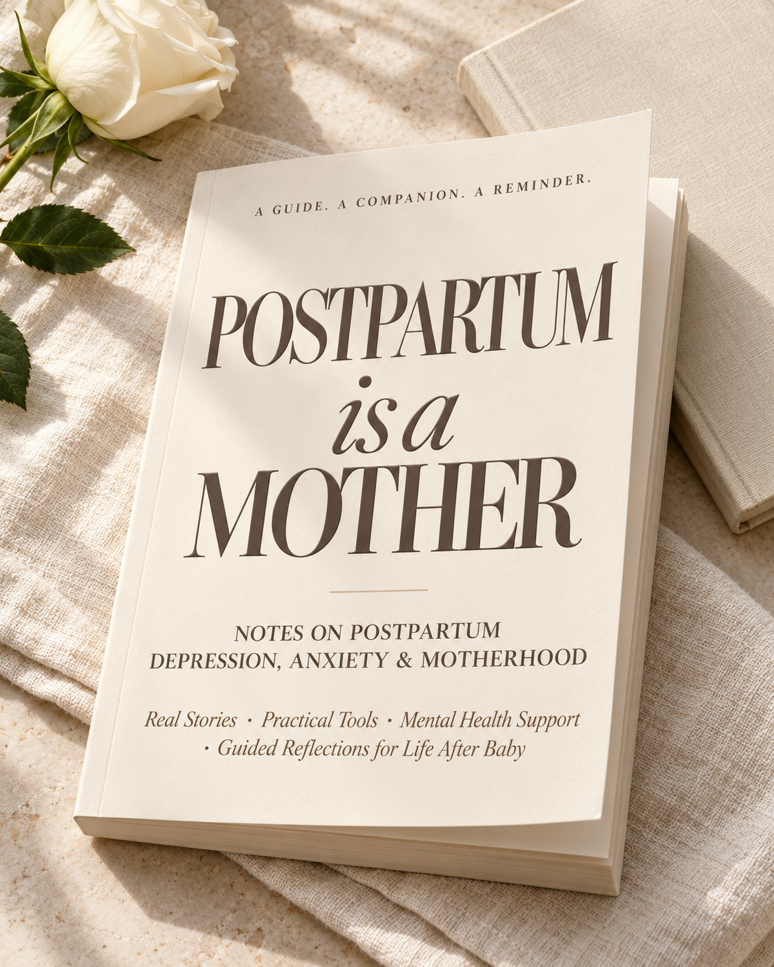 Photographic mockup of an ivory Postpartum Is a Mother paperback on pale stone beside a white rose and a neutral journal